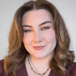 Photograph of a woman smiling, with brown hair and a maroon top on