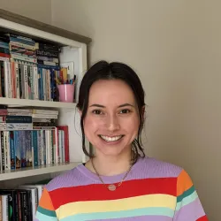 White woman with brown hair tied back smiling with colourful stripey top on