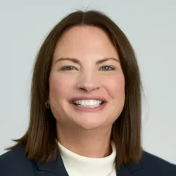 White woman with brown hair  wearing a white top and jacket, smiling