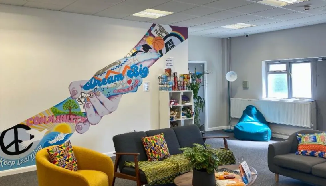 Photograph of inside the hub, a room with a warm and bright environment and a colourful mural on the wall.