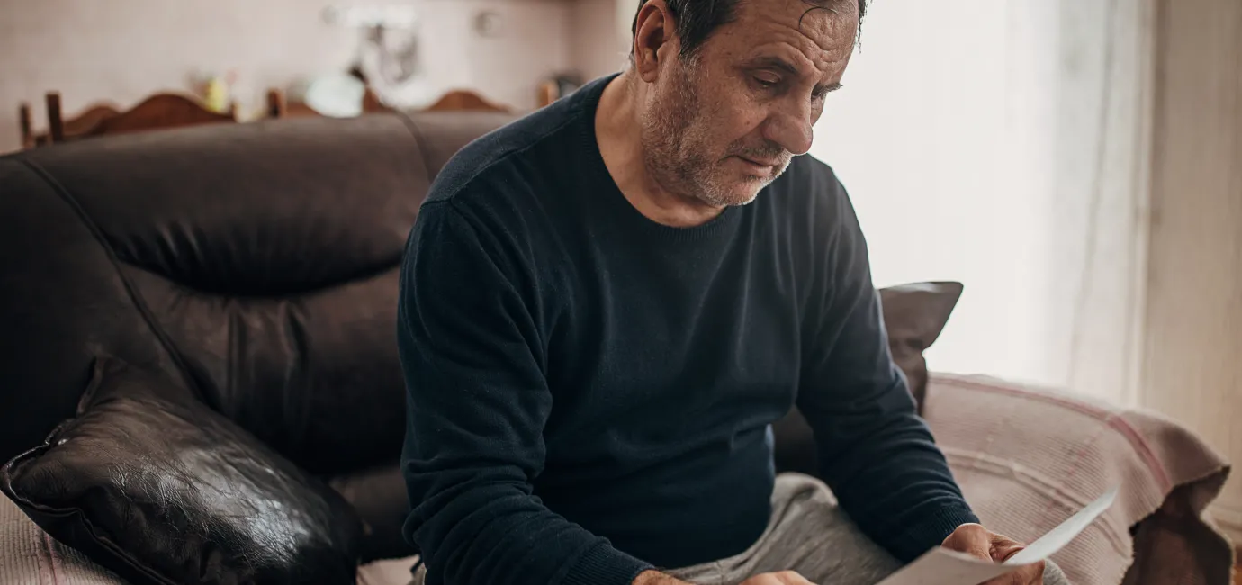 Photograph of a man sat on a sofa looking at a letter